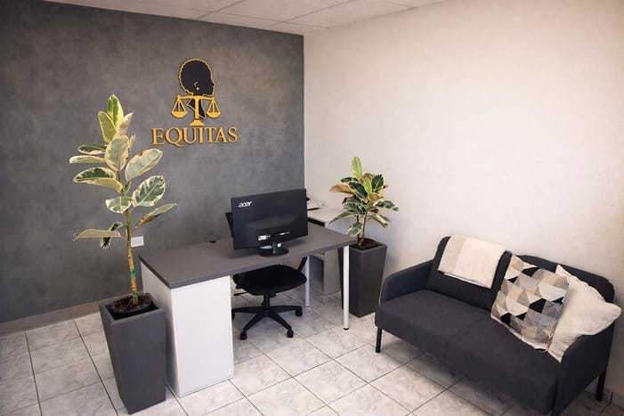Recepción con el logo dorado de Equitas, plantas y un sofá